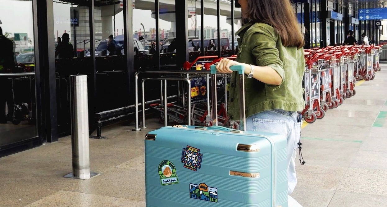 Una chica entrando al aeropuerto con una maleta grande