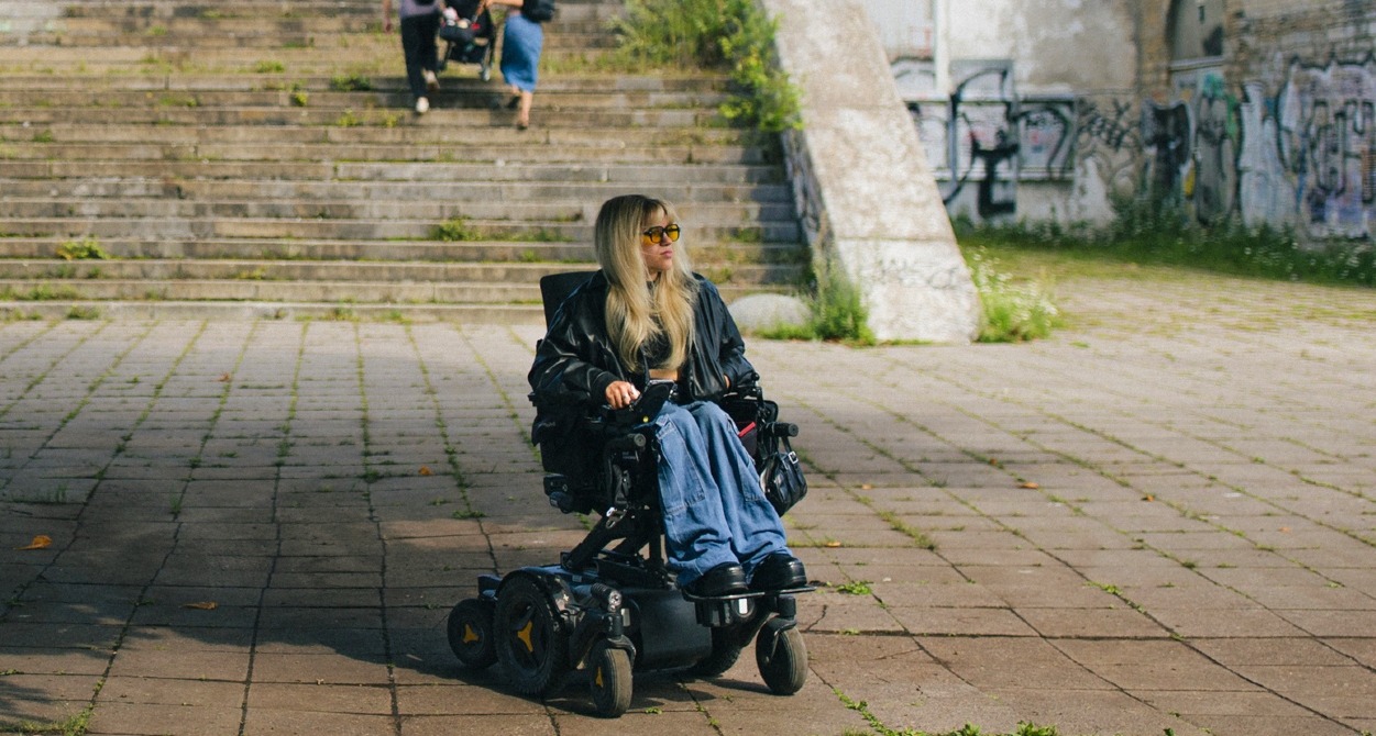 Una chica en silla de ruedas y unas escaleras detrás