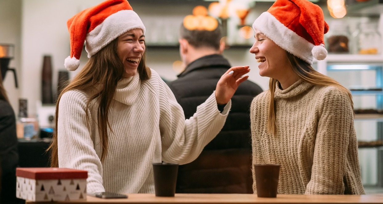 dos chicas tomando café y riendo con gorros de papá noel
