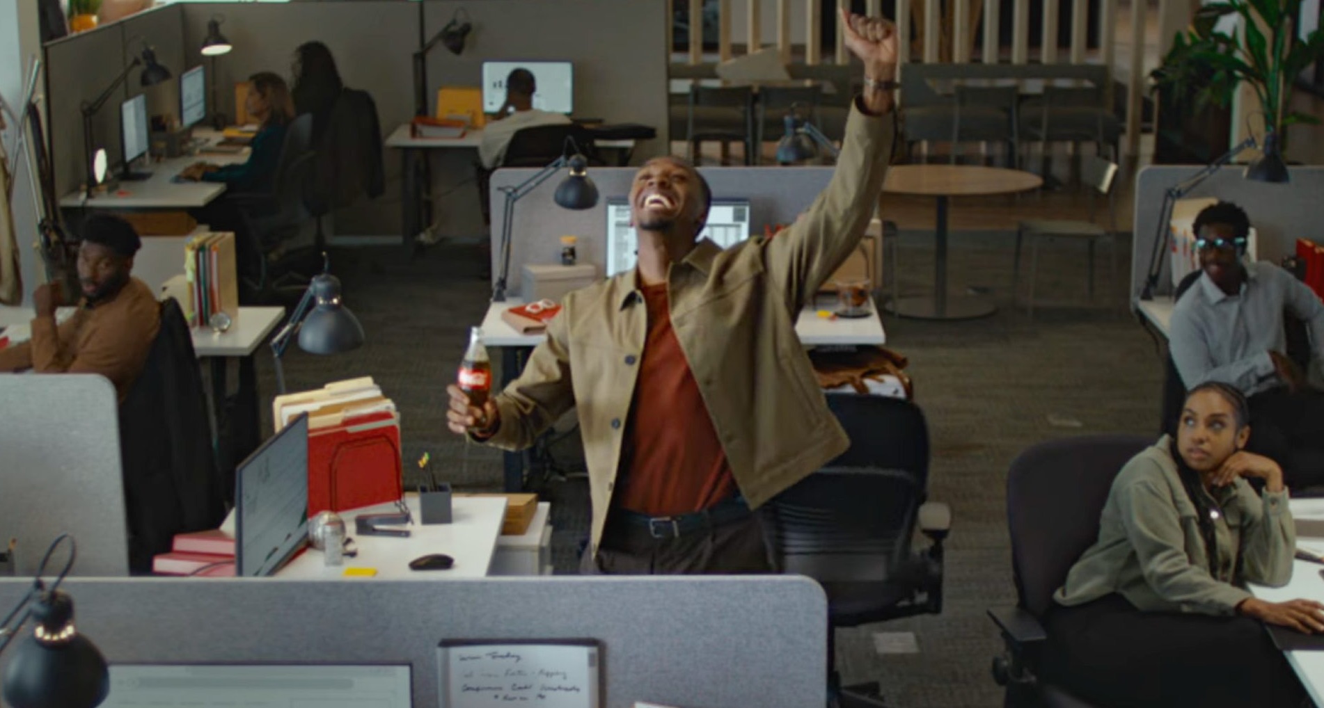 Un hombre en una oficina celebra un gol con una coca-cola en la mano