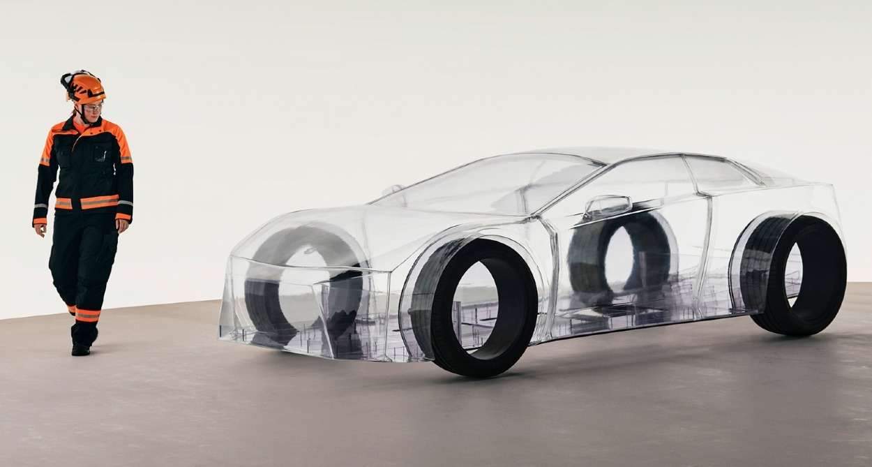 Un ingeniero pasa al lado del coche transparente al que solo se le ven las cuatro ruedas negras