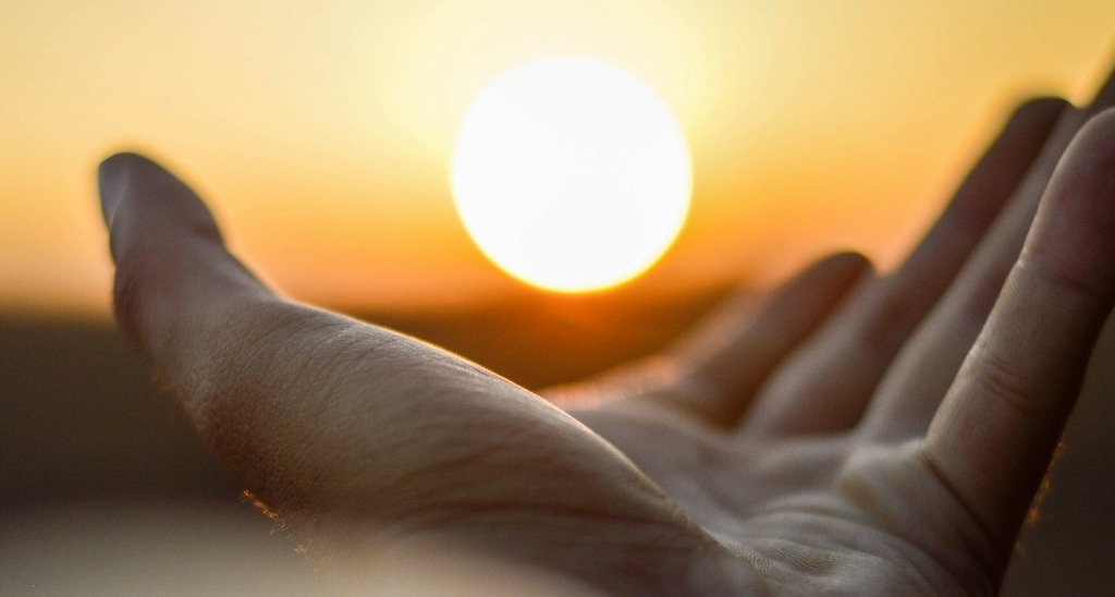 Mano alzada con sol al fondo