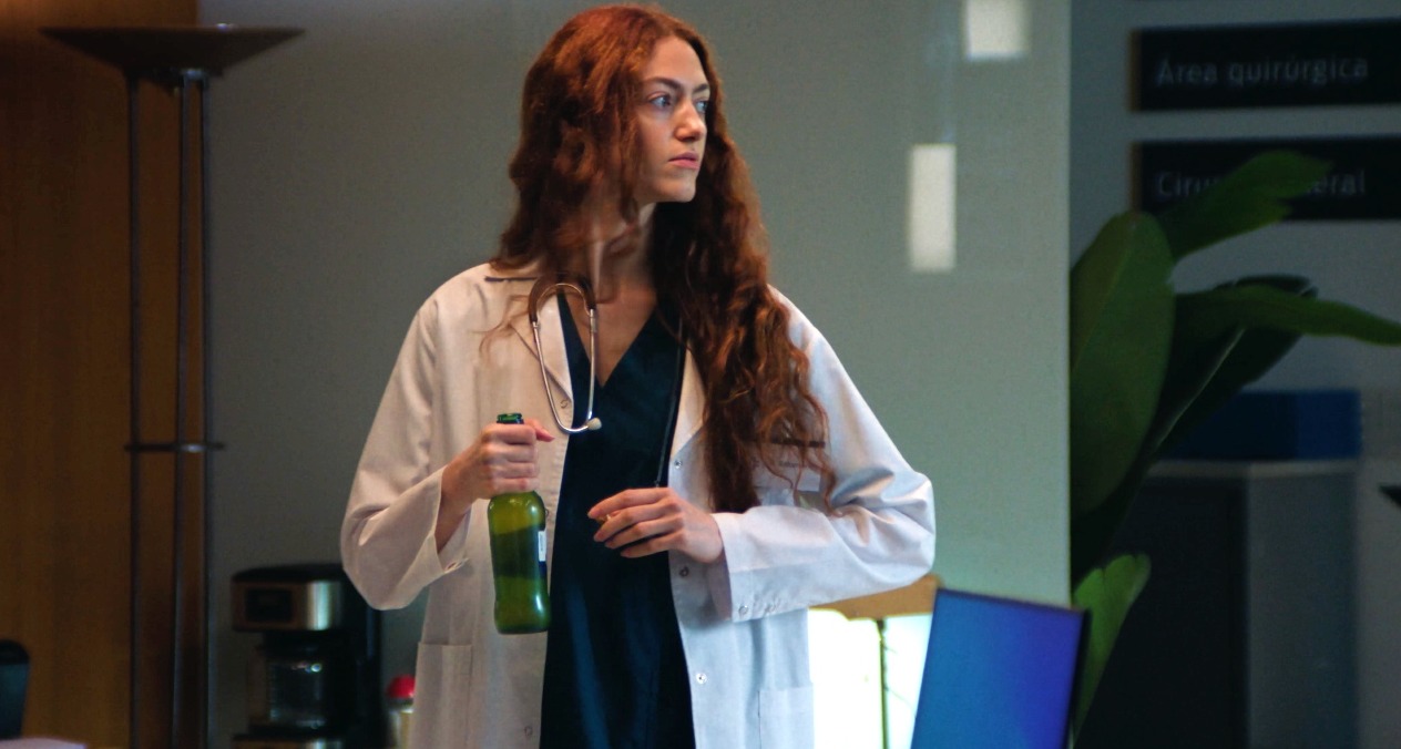 Una doctora con bata abriéndose una cerveza en el despacjho