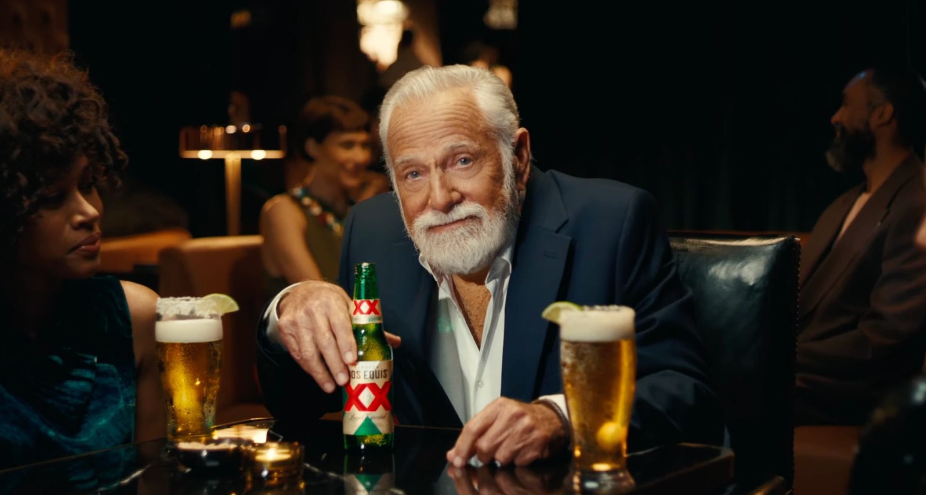 Hombre con barba blanca bebe cerveza Dos Equis en un bar
