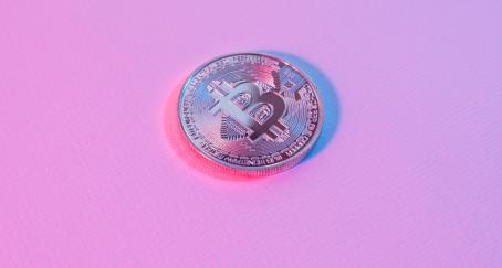 Moneda con símbolo de bitcoin sobre fondo rosa