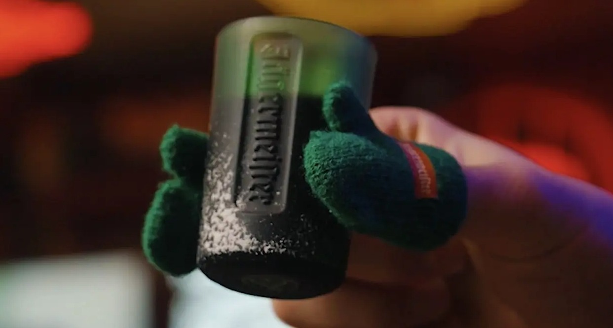 Una mano sosteniendo un chupito con guantes en el dedo pulgar e índice