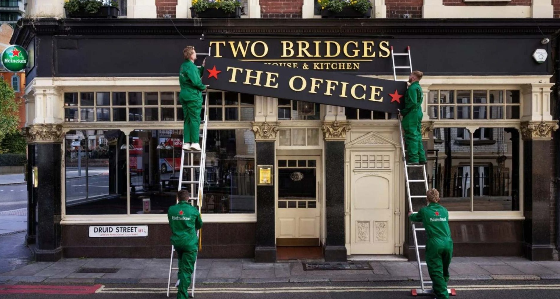 Trabajadores con monos de Heineken colocan un cartel en la fachada de un pub