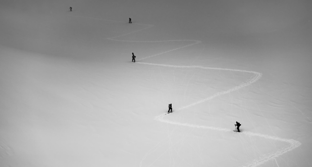 Una montaña con 5 esquiadores de fondo subiendo por el camino que ha trazo el primero