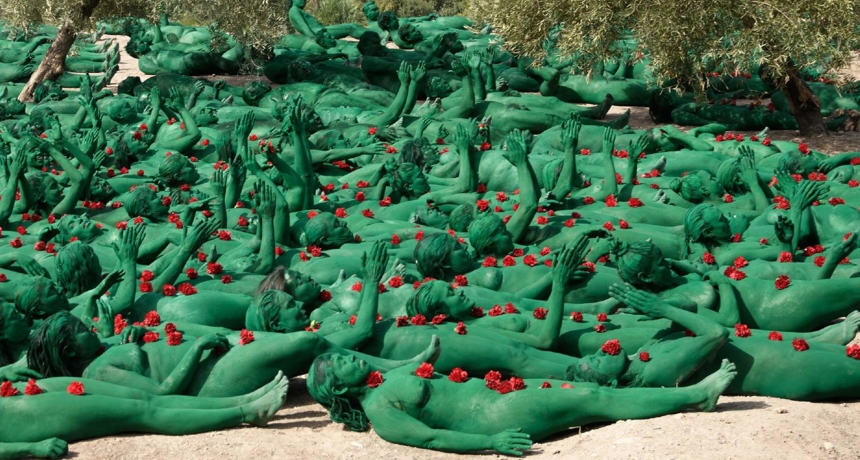 personas con el cuerpo pintado de verde tumbadas en el suelo en el campo