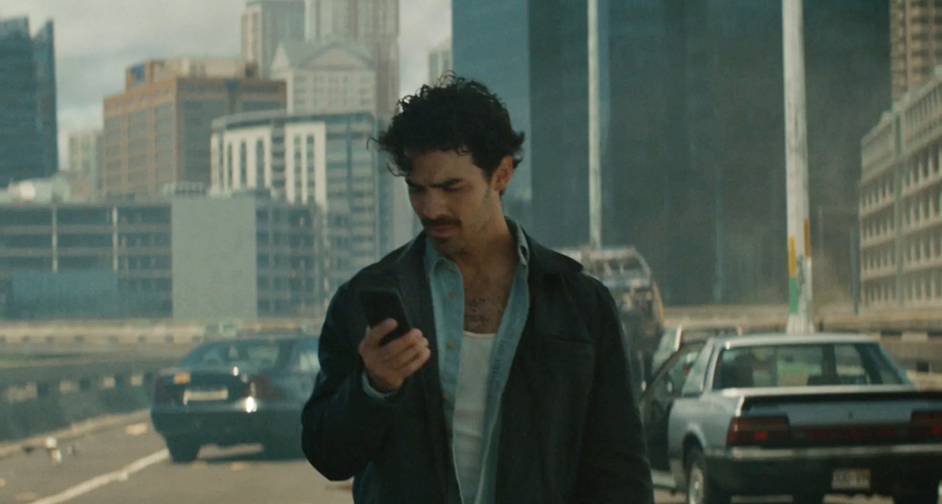 Joe Jonas mirando un teléfono móvil en una ciudad arrasada y sin habitantes