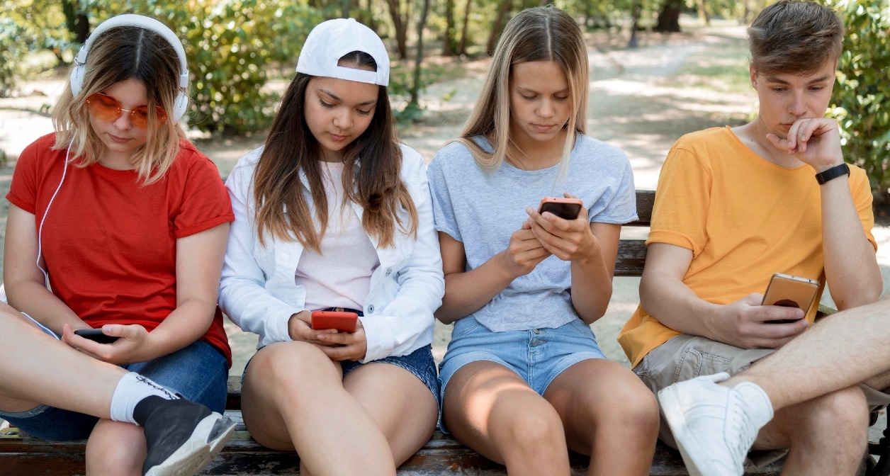 Jóvenes sentados en un banco del parque mirando el teléfono