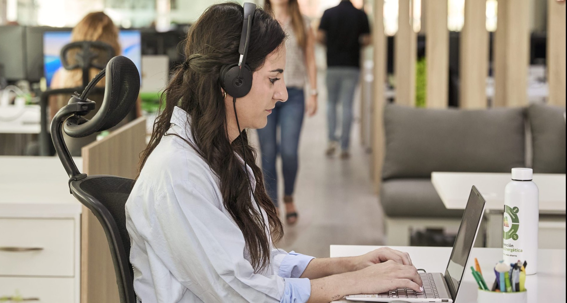 Mujer trabajando delante del ordenador con auriculares