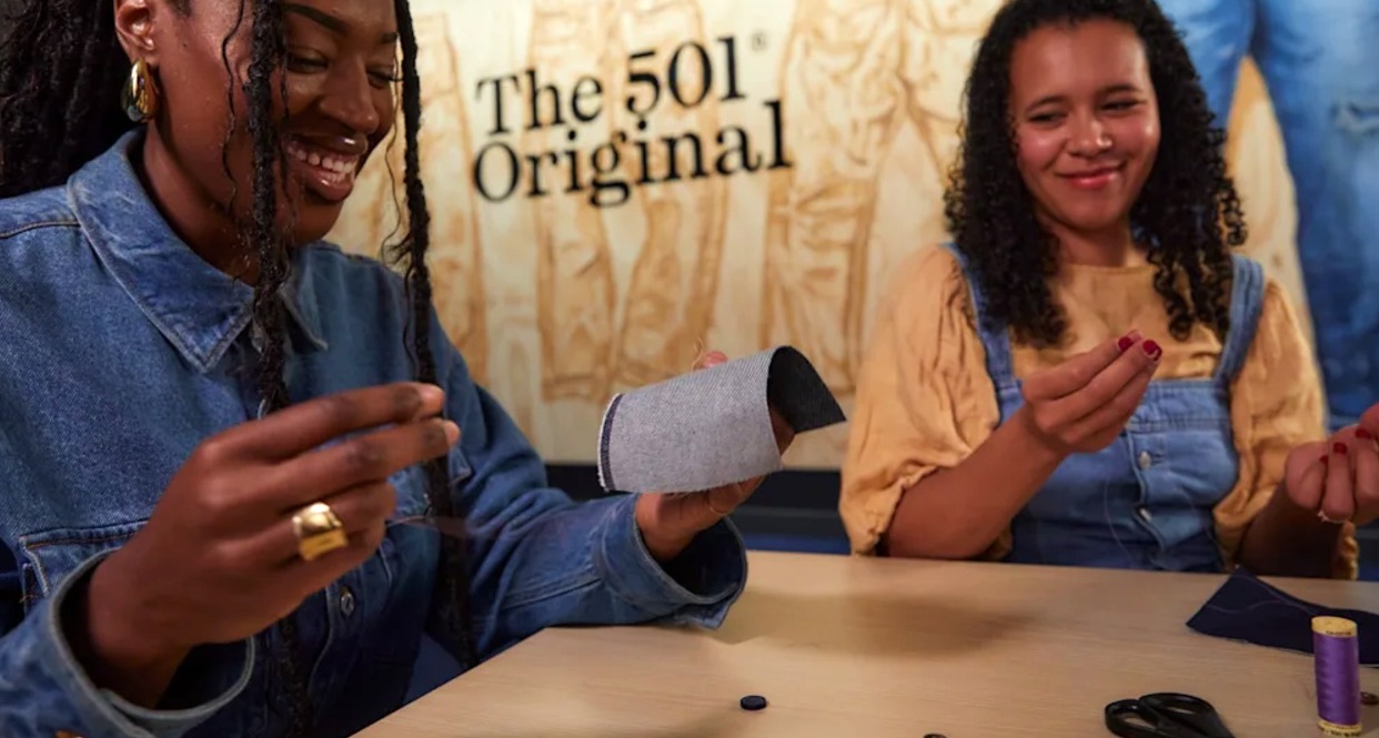 Dos chicas con aguja e hilos riendo mientras intentan coser