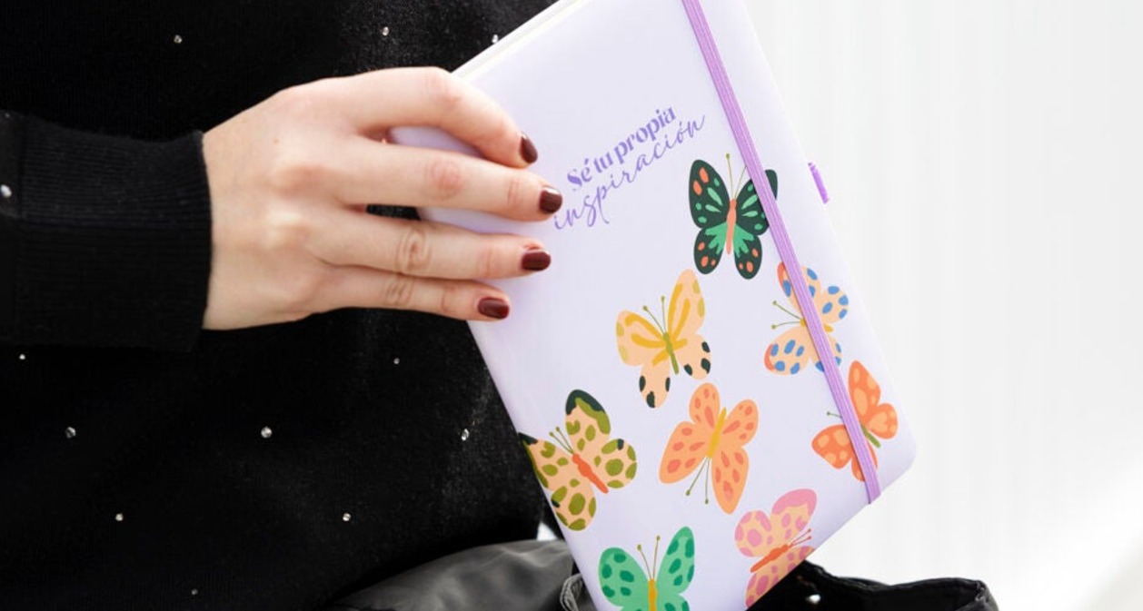 Una mano de mujer sosteniendo una libreta en la que se lee la frase "Sé tu propia inspiración"