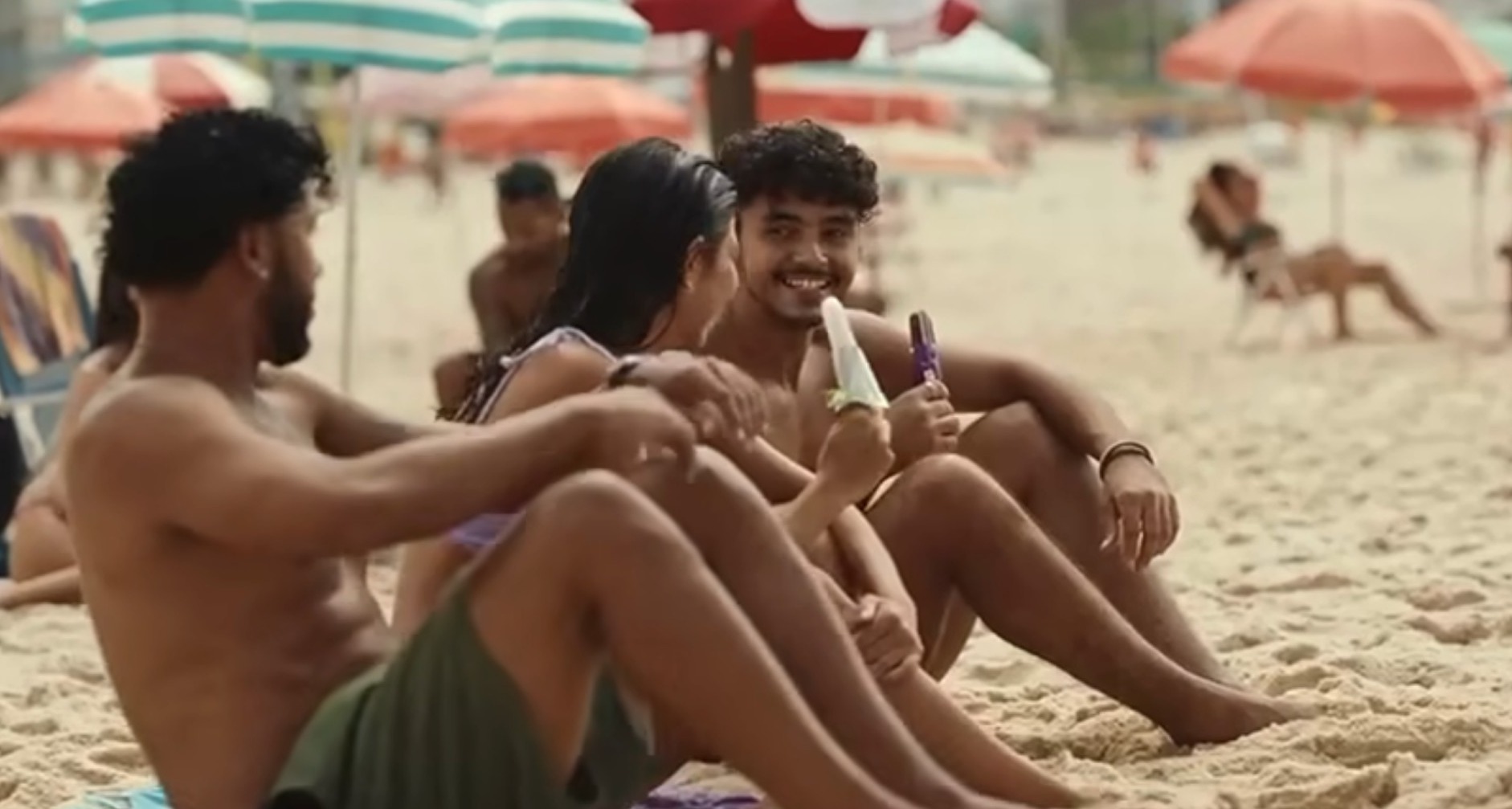 Tres personas jóvenes comen helado en una playa