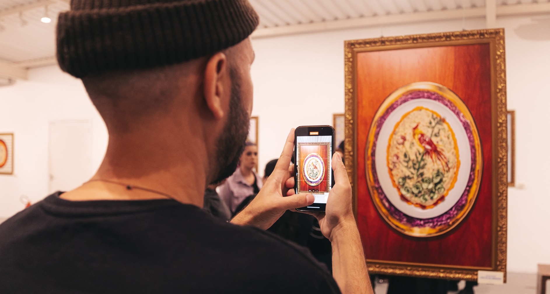 Persona joven de espaldas haciendo una foto con su móvil a uno de los cuadros de ensalada de patatas, de la exposición "Food Art", integrada en la campaña "Mayonismo" de Hellmann's Brasil