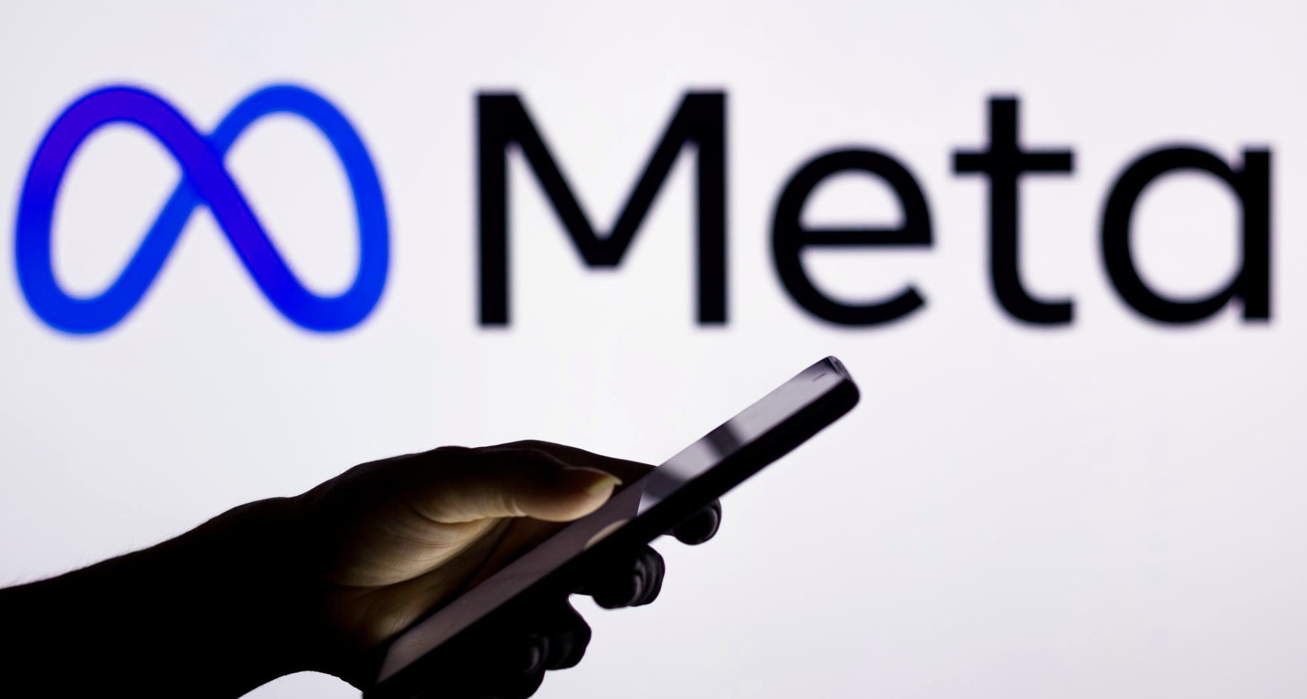 Mano sujetando un móvil con el logo de Meta detrás