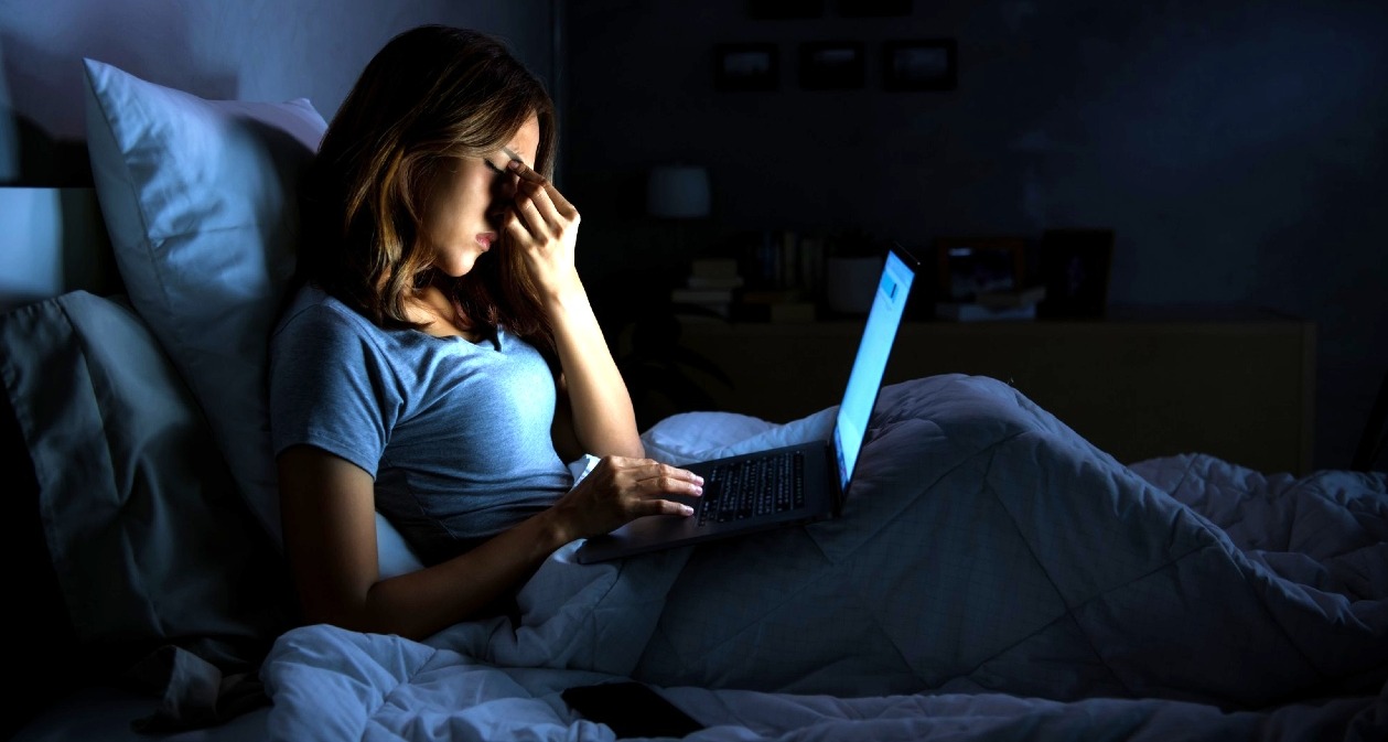 Una mujer en la cama con gesto de preocupación sosteniendo el portátil en las piernas