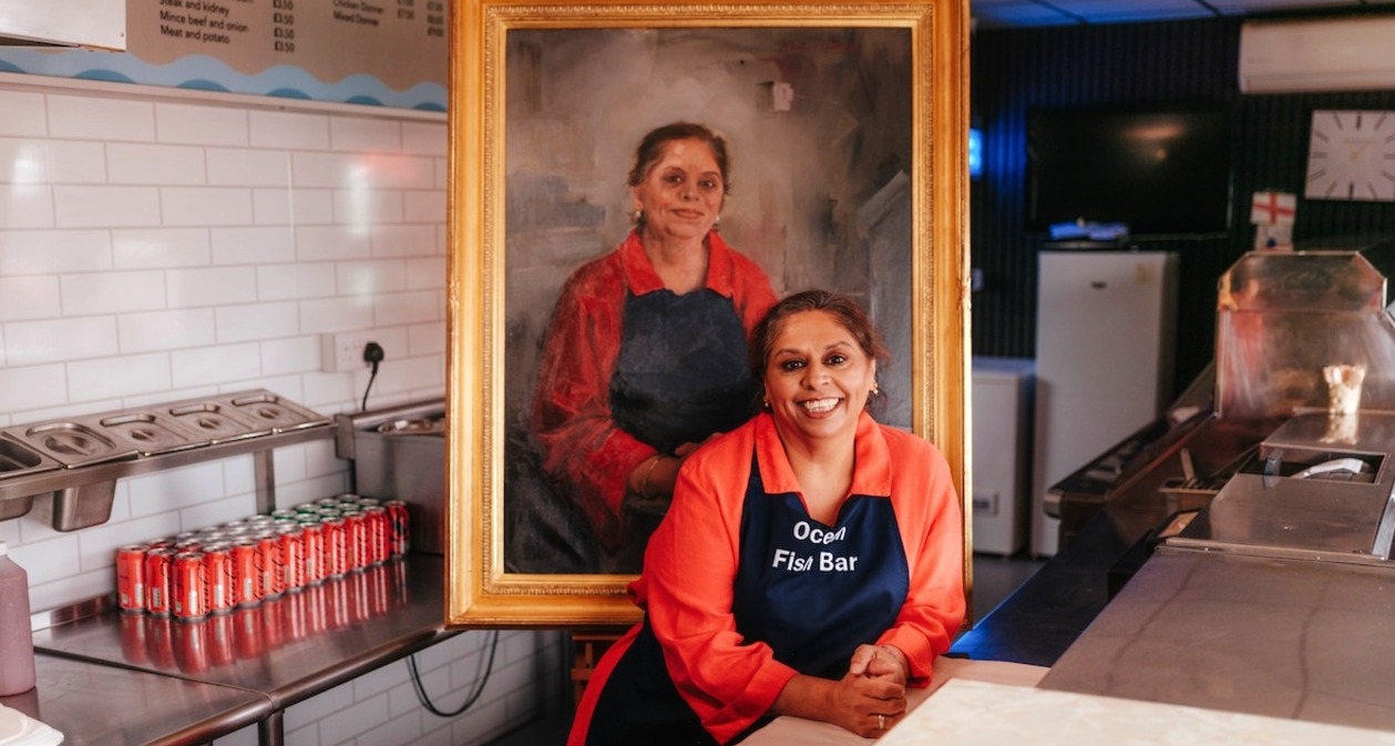 Una mujer en la cocina de su restaurante posando junto a su cuadro