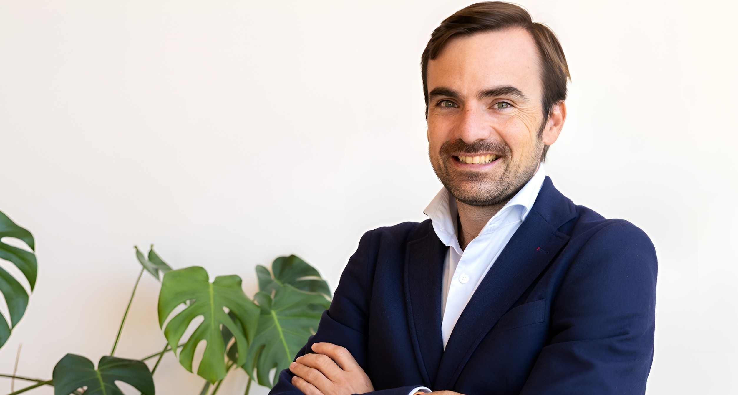 Posado corporativo de Nacho Navarro en traje y con los brazos cruzados al lado de una planta