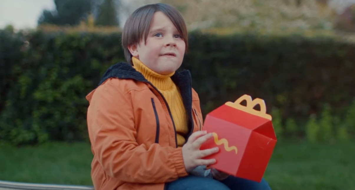 niño sentado con una caja del happy meal y cara de confusión