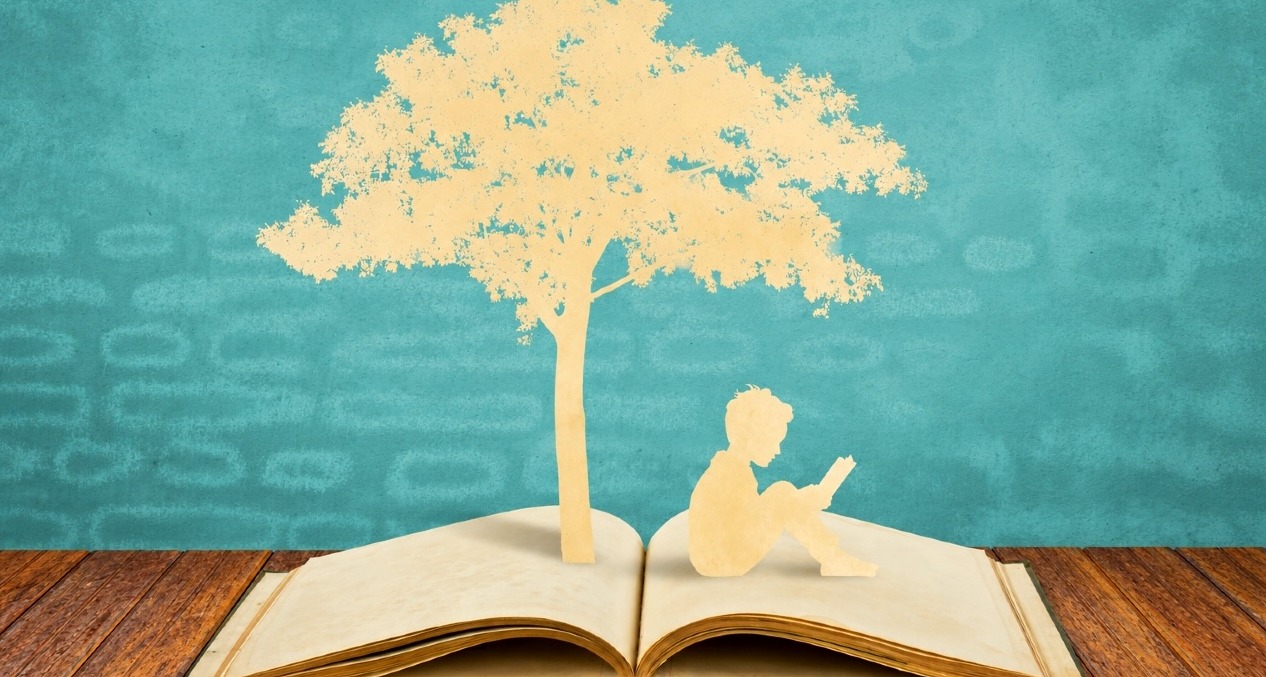 Un recorte de papel que sale de un libro y muestra la silueta de un árbol y un niño sentado leyendo