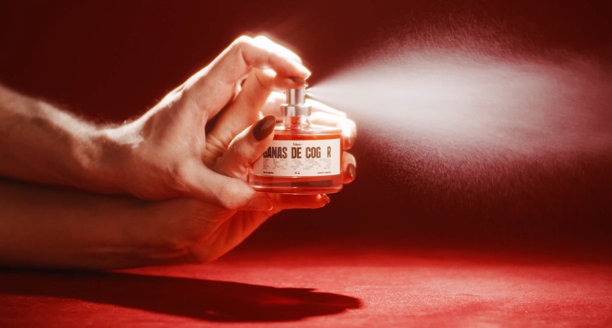 Las manos de un hombre y una mujer sosteniendo el bote del que sale perfume
