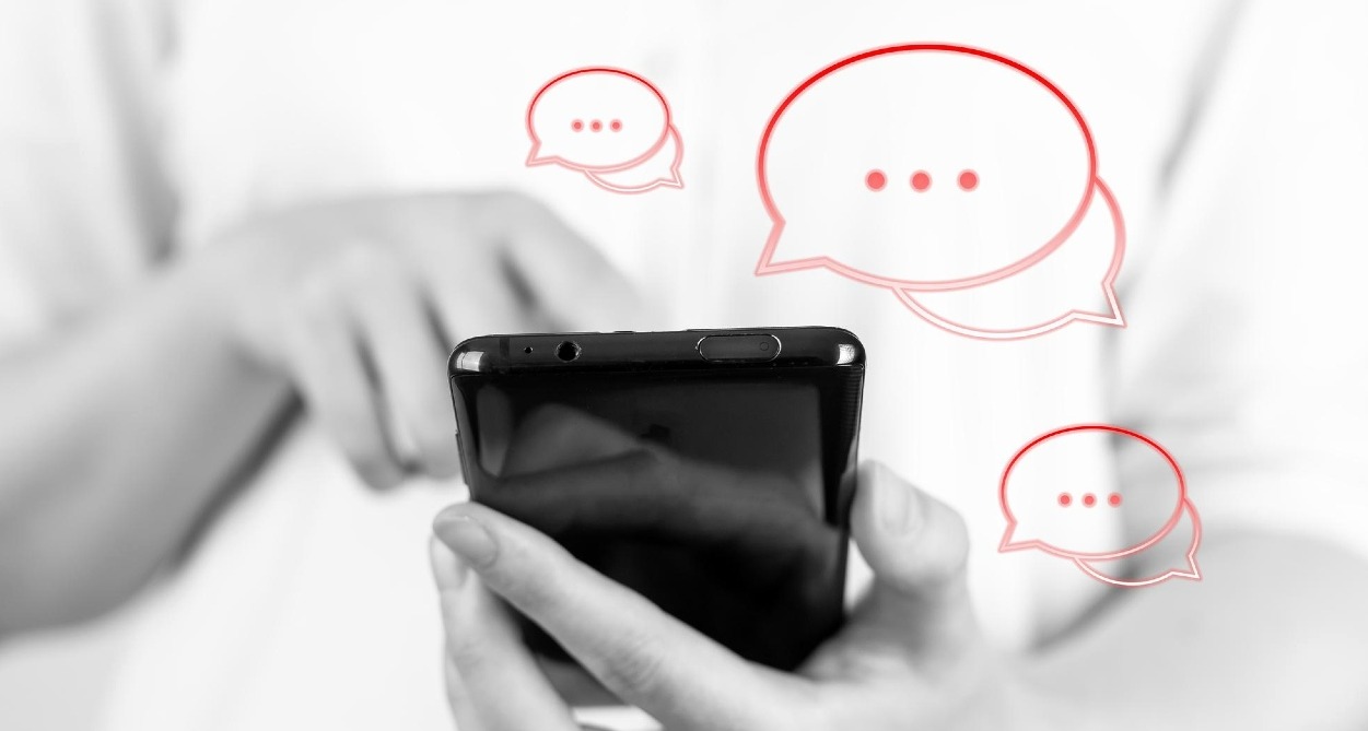 Unas manos sosteniendo un móvil en blanco y negro y bocadillos de conversación en rojo alrededor