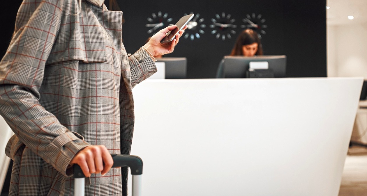 Una mujer con maleta en la recepción del hotel usando el móvil