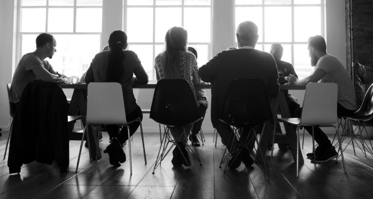 Una imagen en blanco y negro de personas reunidas en una mesa de oficina