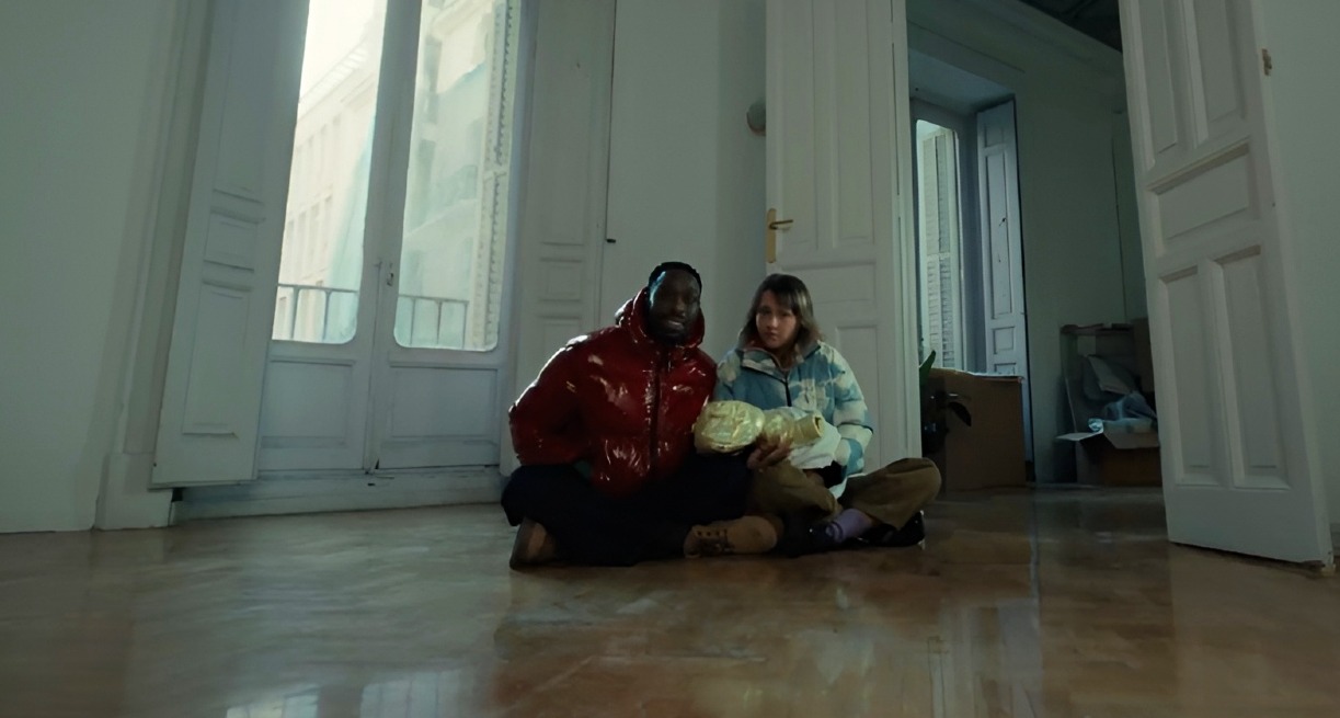 Una pareja sentada en el suelo de un salón vacío con su bebé en brazos
