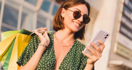 Chica joven con bolsas en la mano mira su teléfono móvil