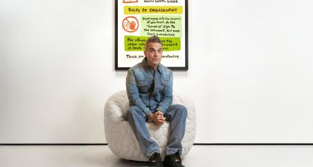 Robbie Williams se refugia en el diseño para hablar de salud mental con “The Introvert Chair” El músico Robbie Williams sentado en la butaca blanca junto al manifiesto para introvertidos