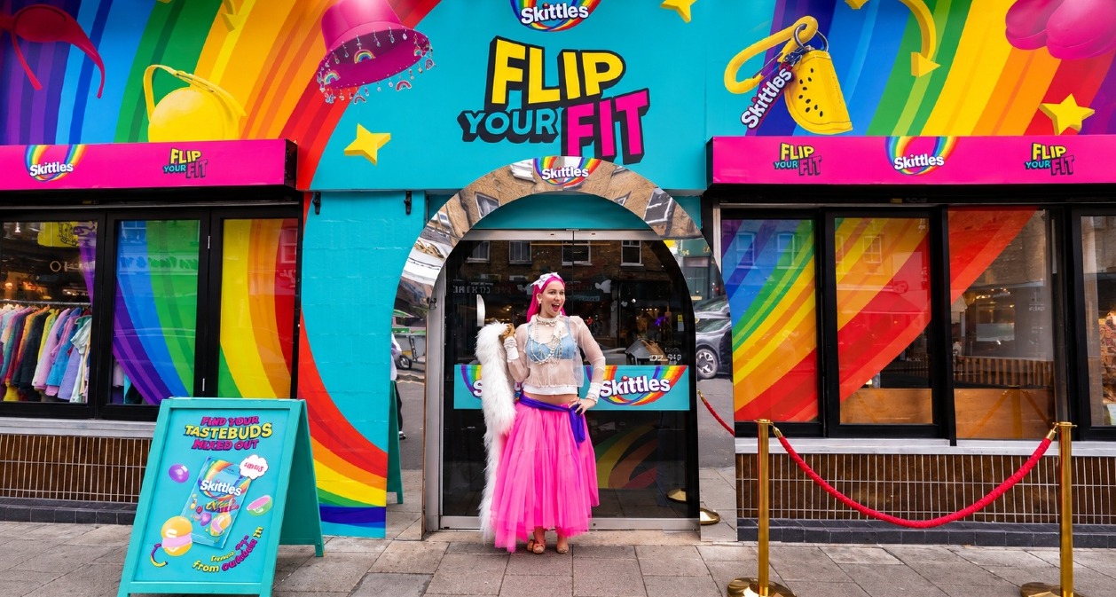 Una chica vestida de colores frente a la pop-up de Skittles