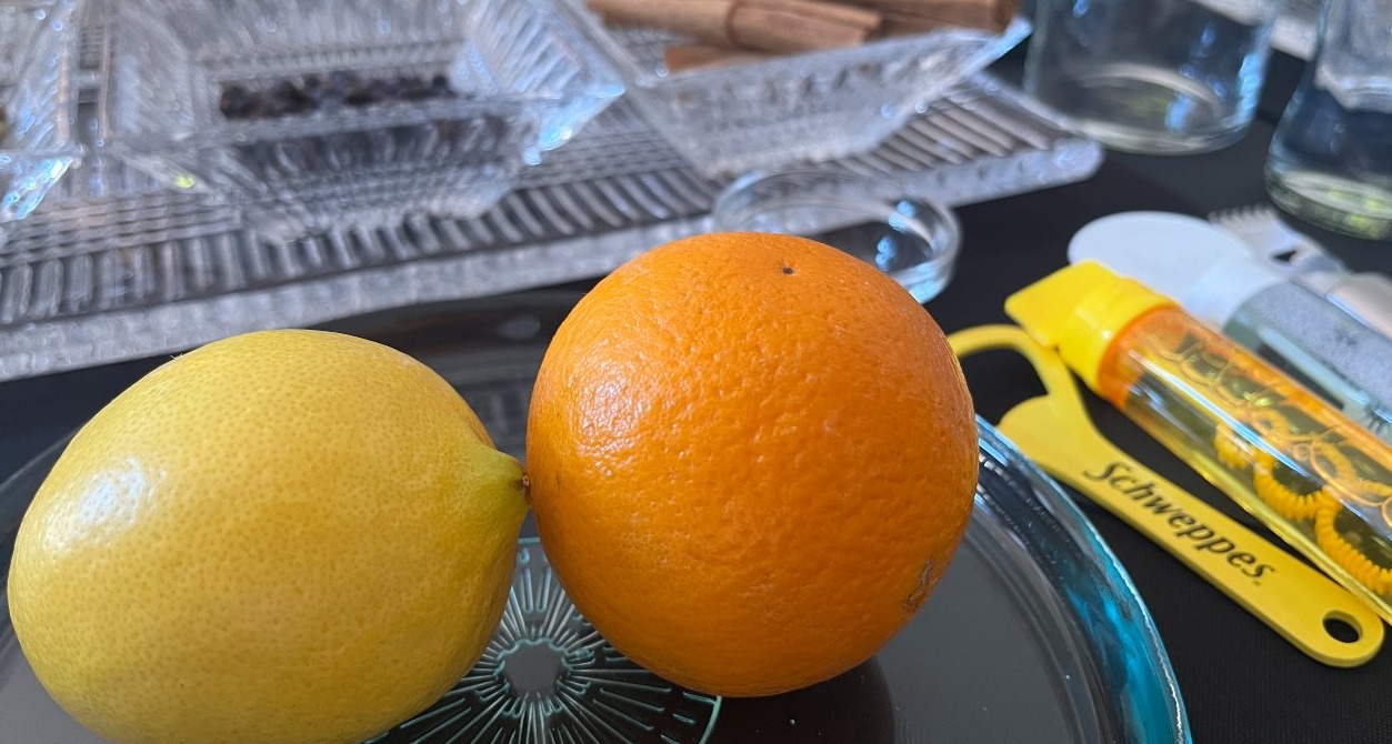 un bodegón con limón, naranja, especias, un abridos, pomperos, antifaz y papel de burbujas con un pelador