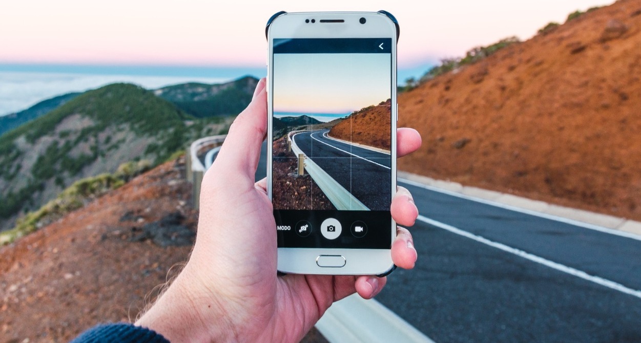 Una mano sosteniendo un móvil para hacer una foto del paisaje de una carretera de montaña