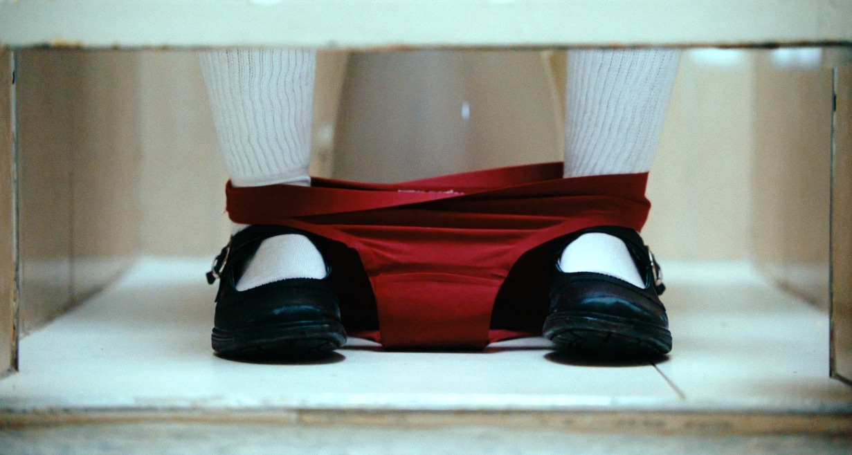 Los pies de una niña en el aseo con las braguitas rojas bajadas