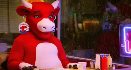 La vaca sentada en un bar con una cristalera lluviosa y el rostro triste