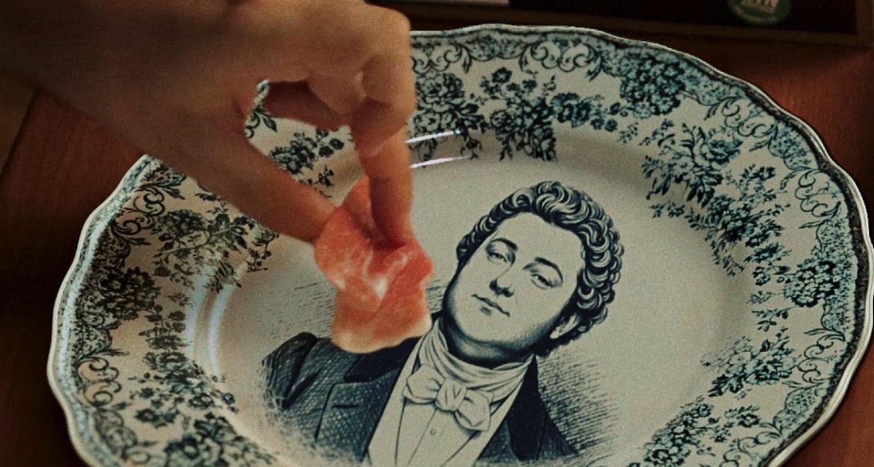 una mano cogiendo un trozo de jamón de un plato de porcelana con ilustraciones en azul