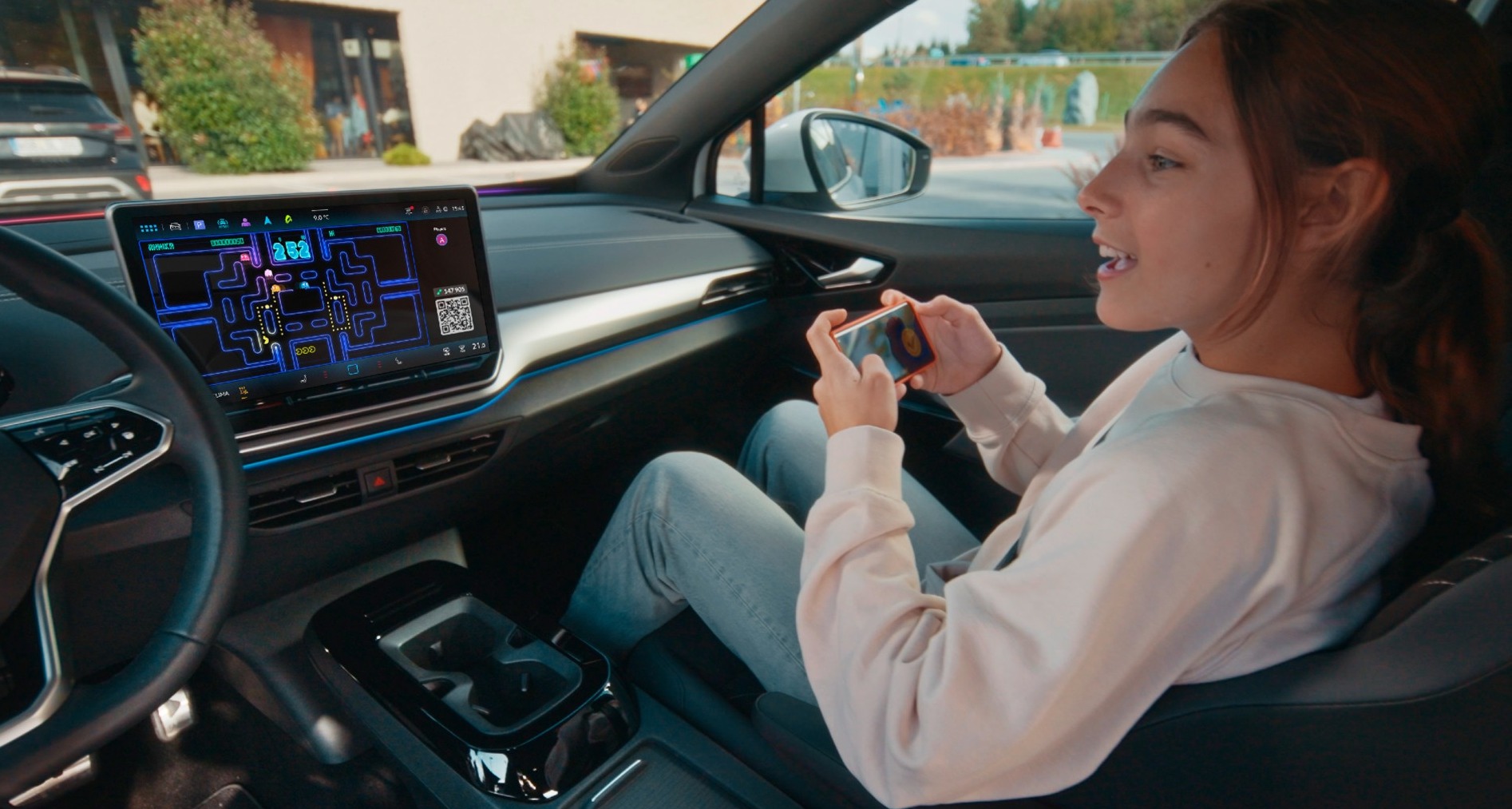 Volkswagen integra el videojuego “Pac-Man” y mejora la experiencia social de sus coches Una joven jugando a Pac-Man con el móvil desde el asiento de copiloto de un coche Volkswagen