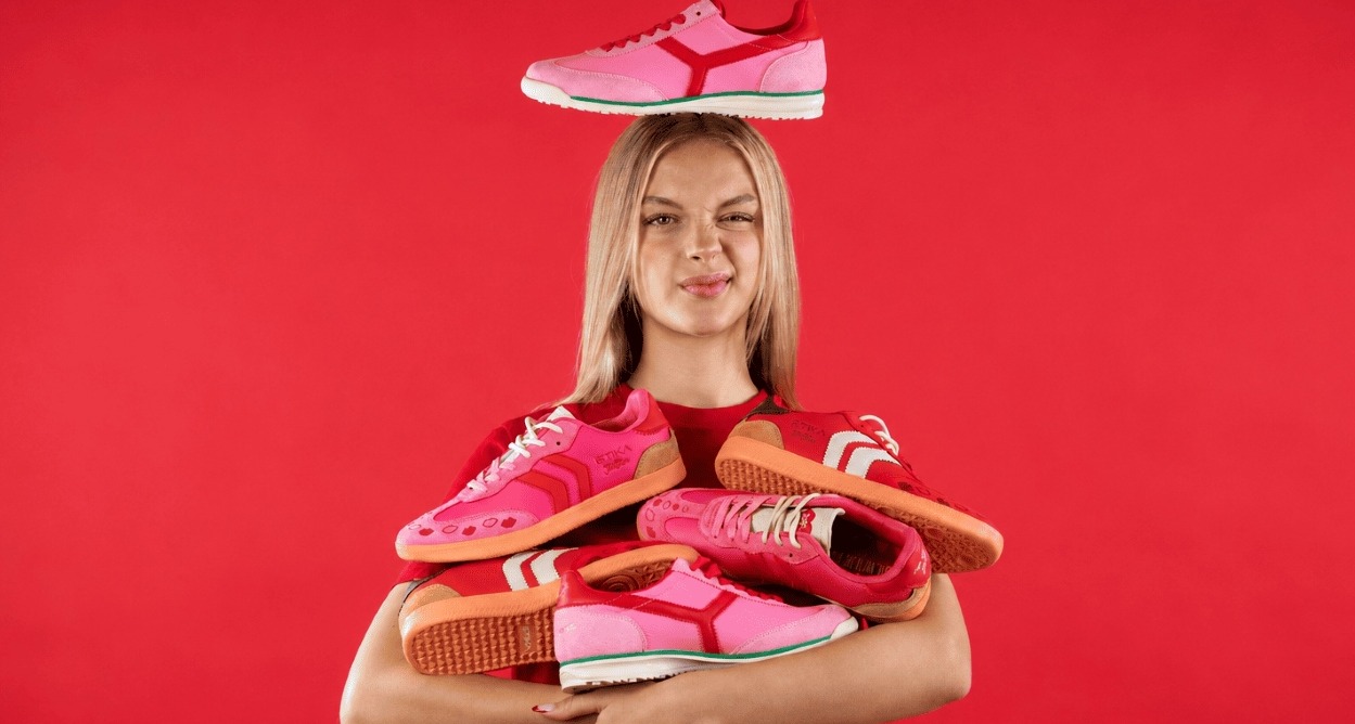 Una chica con muchas zapatillas entre los brazos, una en la cabeza y el fondo rojo