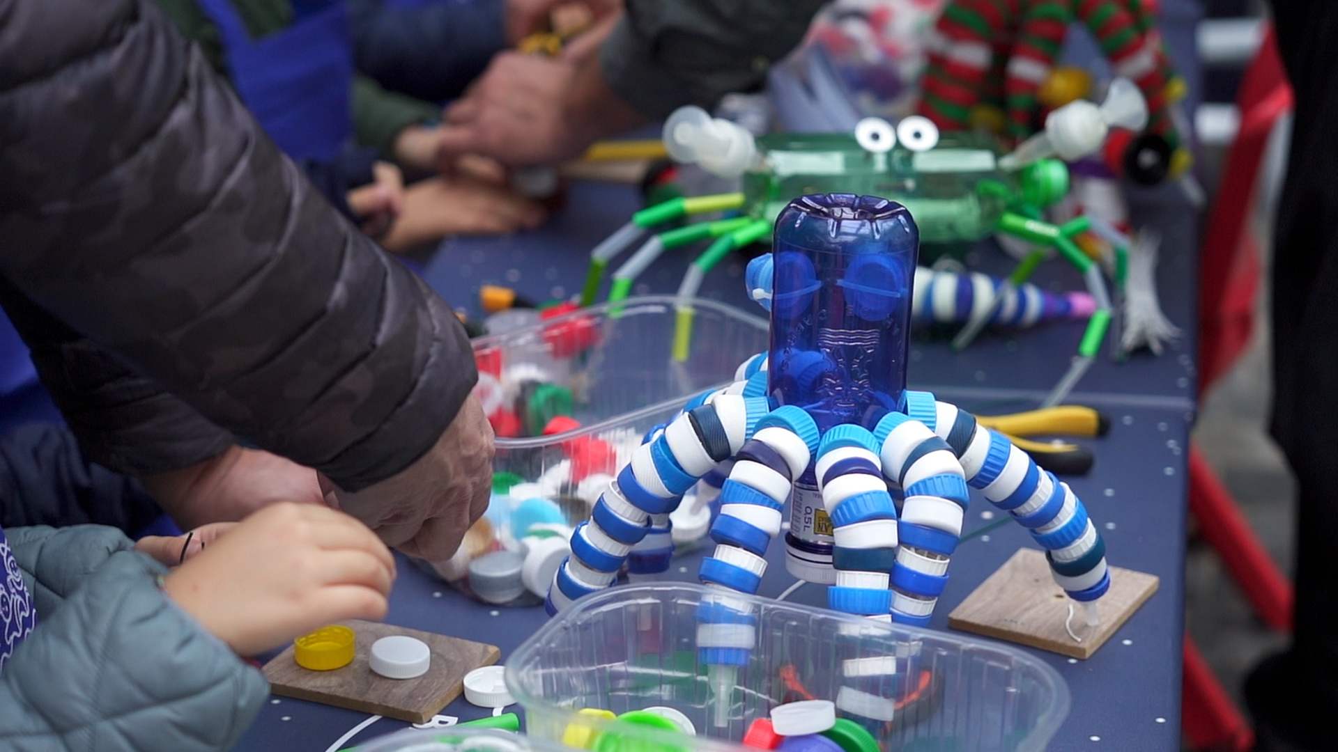 Un juguete elaborado con residuos de plástico y manos de diferentes personas trabajando con estos objetos.