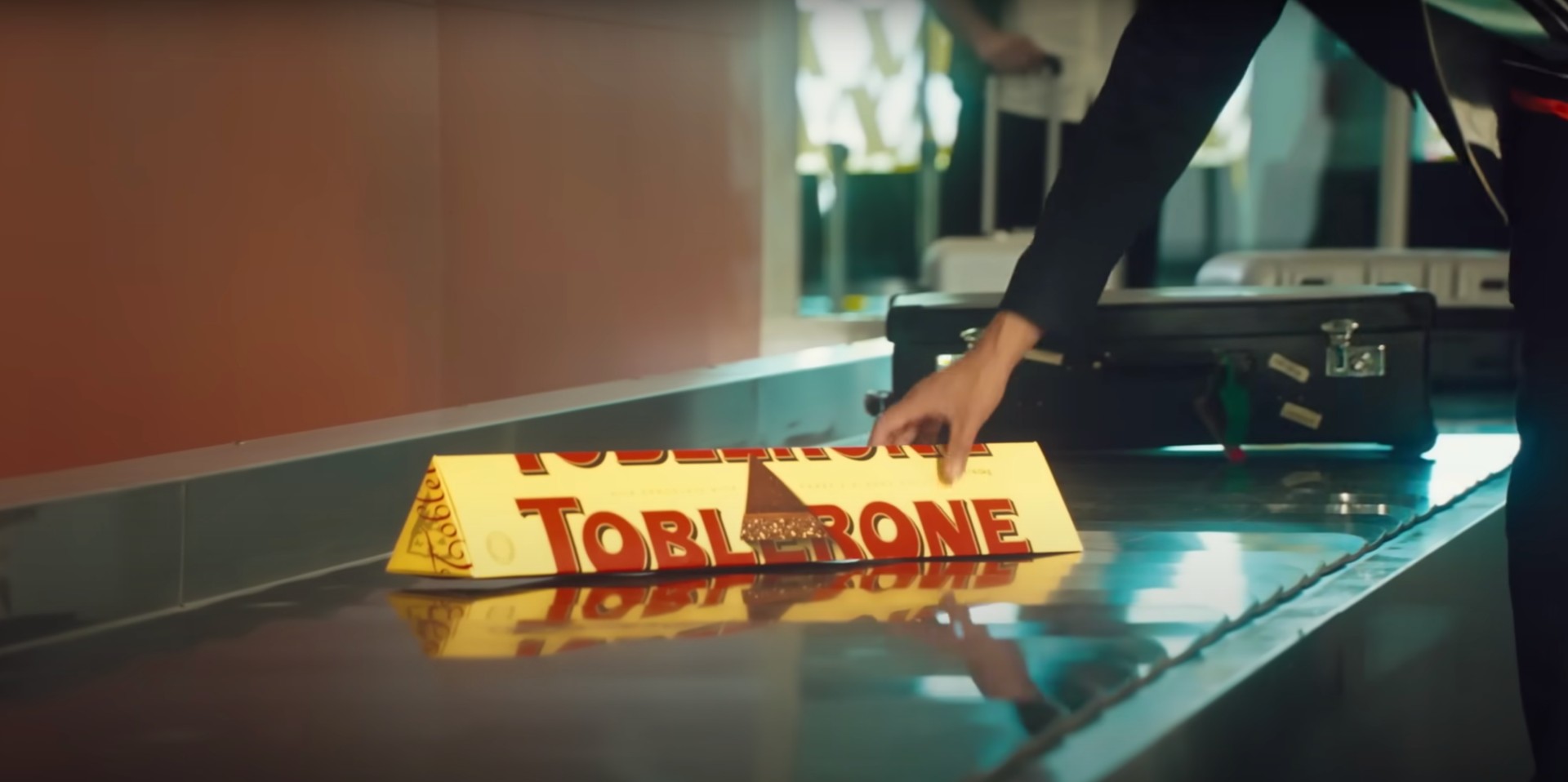 Una mano coge un gran envase de Toblerone de una cinta de equipaje en una imagen del spot.