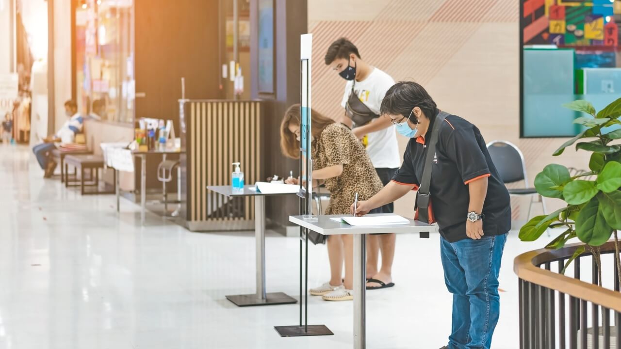 Gente firmando en mostradores con pantallas y mascarilla